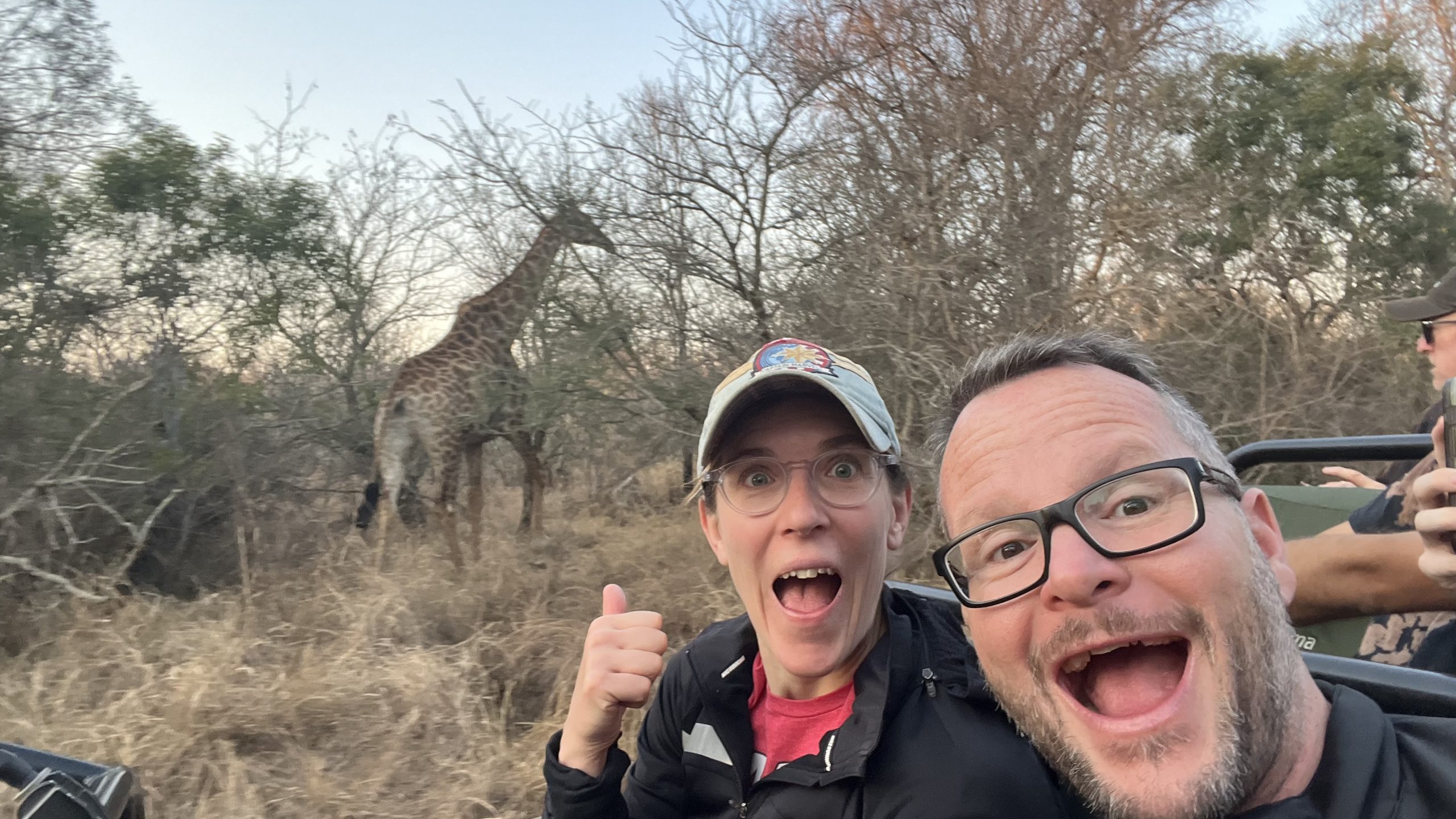 Giraffe walking through dry bushland on a South African safari, captured from close range with natural vegetation in the background.